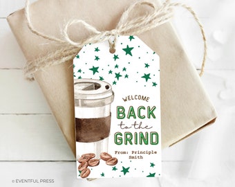 May include: A gift tag with a watercolor illustration of a coffee cup and beans. The tag reads "Welcome Back to the Grind" in green and brown text, with green star accents. The tag is tied to a wrapped gift with twine.