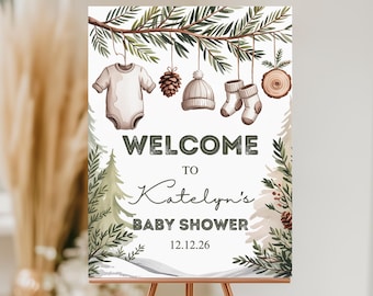 Könnte beinhalten: Willkommensschild für eine Babyparty mit Aquarelldesign. Es zeigt einen Zweig mit Babykleidung und Tannenzapfen. Das Schild lautet "WELCOME to Katelyn's BABY SHOWER 12.12.26" in einer dekorativen Schriftart, mit Winterthema.
