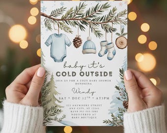 Könnte beinhalten: Einladung zur Babyparty mit Winterthema. Die Einladung zeigt einen blauen Strampler, einen Tannenzapfen, eine Mütze und Socken, die an einem Ast hängen. Der Text lautet "baby it's cold outside" und lädt Gäste ein.