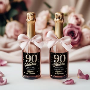 May include: Two champagne bottles with gold foil tops and pink bows. Each bottle has a black label with the text "90 and Fabulous" and "Thank you for coming to Kathleen's 90th Birthday."