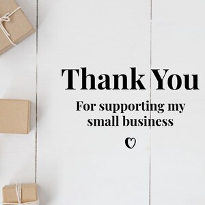 May include: An overhead shot shows several small, brown gift boxes arranged on a white wooden surface. Some boxes are tied with twine. The words "Thank You" are displayed in a bold, black font, followed by "For supporting my small business" and a heart symbol.