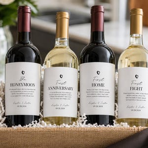Pode incluir: Quatro garrafas de vinho numa cesta trançada, cada uma com um rótulo branco com um pequeno ícone de coração e texto personalizado. Os rótulos dizem The Honeymoon, First Anniversary, First Home e First Fight, com Kaylee & Justin e 09.28.2024.