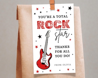 May include: A white gift tag with the words "YOU'RE A TOTAL ROCK STAR" in red and black. A red guitar illustration is featured. The tag is decorated with red and black stars and is attached to a brown paper bag with a wooden clip.