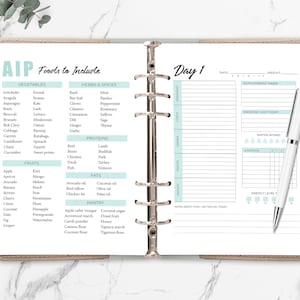 May include: A light brown planner with a light blue and white design. The planner has a section for "AIP Foods to Include" with a list of vegetables, herbs and spices, proteins, fats, and pantry items. The planner also has a section for "Day 1" with sections for date, weight, supplements taken, exercise, water intake, symptoms, and energy level.