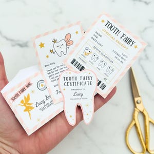 Può includere: Una collezione di articoli a tema Fatina dei Denti, tra cui un certificato, una ricevuta e una lettera. Il certificato ha la forma di un dente e la ricevuta presenta una tabella delle condizioni dei denti. Gli articoli sono decorati con stelle e una fata.