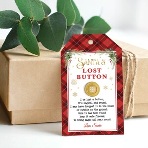 May include: A gift tag with the text "Santa's Lost Button" in gold lettering, featuring a gold button illustration. The tag has a red plaid pattern and a poem. The gift box is wrapped in brown paper and twine.
