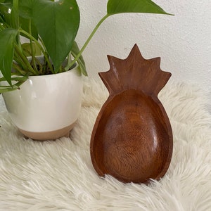 May include: A wooden pineapple-shaped bowl with a brown finish. The bowl is sitting on a white fluffy surface.
