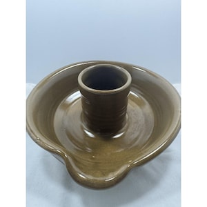 May include: A round, brown glazed ceramic baking dish featuring a central vertical cylinder and a small pouring spout on the rim. The surface has a smooth, glossy finish with subtle horizontal ridges visible on the exterior of the central column.