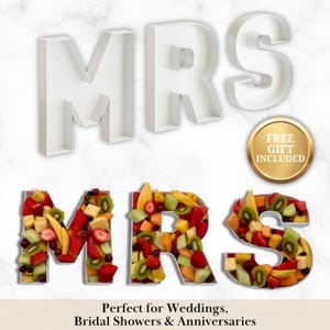 May include: White "MRS" letters and fruit-filled "MRS" letters are displayed. The fruit-filled letters are composed of various fruits, including strawberries, kiwi, and mango. A gold-colored circle with the text "FREE GIFT INCLUDED" is also present. The text "Perfect for Weddings, Bridal Showers & Anniversaries" is at the bottom.
