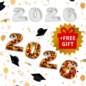 May include: A celebratory graphic with the year "2026" in white, with the numbers filled with a colorful fruit salad. Graduation caps and confetti surround the numbers. A gold starburst with a gift box and the words "+ FREE GIFT" is also present.