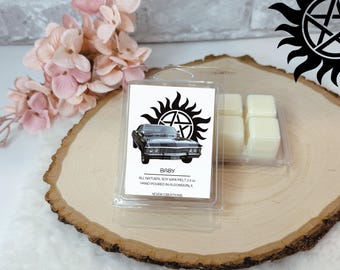 May include: A clear plastic package containing six square wax melts and a label with a black car graphic and the word "BABY". The label also includes a black sunburst design and text that reads "ALL NATURAL SOY WAX MELT 2.5 oz HAND POURED IN ALGONQUIN, IL".