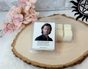 May include: A clear plastic container holding wax melts and a label featuring Sam Winchester. The label reads "Sam Winchester" and "All Natural Soy Wax Melt 2.5 oz Hand Poured in Algonquin, IL". The wax melts are light yellow and in a separate compartment.