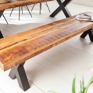 May include: A wooden bench with a natural wood finish and black metal X-shaped legs. The bench is sitting on a white floor.