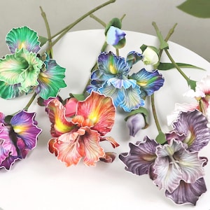 以下が含まれることがあります： 紫、ピンク、オレンジ、青、緑の色合いの、カラフルな人工のアイリスの花のコレクション。 花は白い表面に配置され、緑色の茎とつぼみがあります。 花びらは詳細な葉脈とリアルな外観をしています。