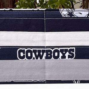May include: A rectangular fabric organizer featuring a navy blue and white design with the word "COWBOYS" in white block letters. The organizer has a star logo and is divided into sections with visible stitching.