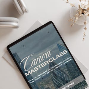Pu&ograve; includere: Un tablet digitale che mostra una grafica con il testo "Canva MASTERCLASS" e lo slogan "La nostra guida completa per creare immagini straordinarie e post virali su Canva - in modo rapido e semplice!" La grafica presenta una citt&agrave; con edifici alti.