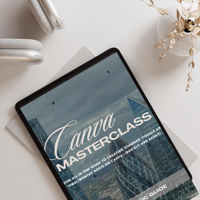 Pu&ograve; includere: Un tablet digitale che mostra una grafica con il testo "Canva MASTERCLASS" e lo slogan "La nostra guida completa per creare immagini straordinarie e post virali su Canva - in modo rapido e semplice!" La grafica presenta una citt&agrave; con edifici alti.