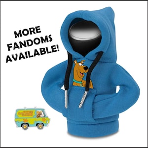 May include: A blue miniature hoodie featuring a Scooby-Doo graphic on the front. The hoodie has black drawstrings and silver-colored aglets. The text "MORE FANDOMS AVAILABLE!" is in the upper left corner. A Mystery Machine van pin is in the lower left.