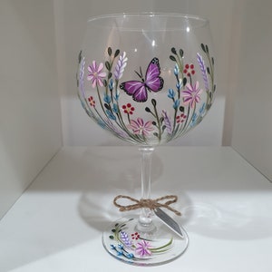 May include: A clear glass gin glass with a hand-painted design of pink, purple and blue flowers and a purple butterfly.