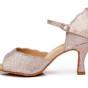 May include: A pair of light beige dance shoes with a rhinestone design and an ankle strap. The shoes have a high heel and an open toe.