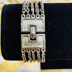 May include: Silver multi-strand chain bracelet with a square clasp. The bracelet has a brushed silver finish and is made of multiple chains.