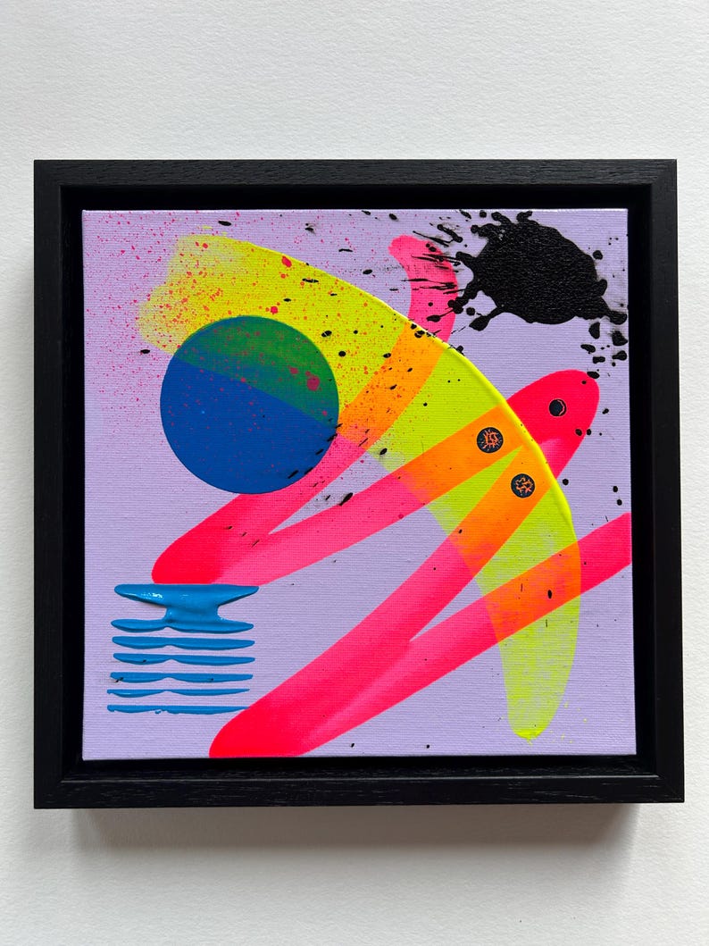 Puede incluir: Un cuadro cuadrado sobre lienzo en un marco negro con fondo violeta claro y formas abstractas. Incluye un c&iacute;rculo azul, pinceladas en rosa ne&oacute;n y amarillo, un dise&ntilde;o de l&iacute;neas horizontales azules apiladas y salpicaduras de pintura negra.