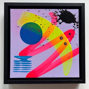 Puede incluir: Una pintura sobre lienzo cuadrada en un marco negro con un fondo morado claro y formas abstractas. Incluye un c&iacute;rculo azul, pinceladas de color amarillo ne&oacute;n y rosa, una salpicadura de pintura negra y un elemento de rayas azules.