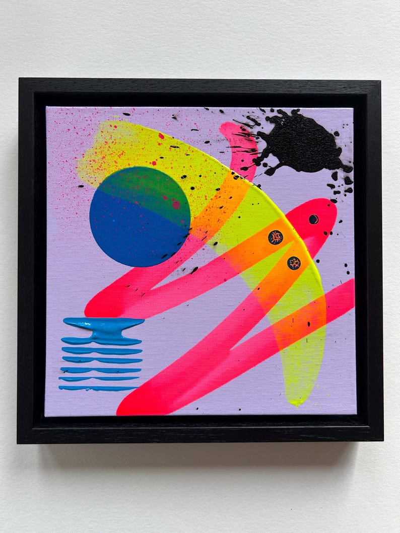Puede incluir: Una pintura sobre lienzo cuadrada en un marco negro con un fondo morado claro y formas abstractas. Incluye un c&iacute;rculo azul, pinceladas de color amarillo ne&oacute;n y rosa, una salpicadura de pintura negra y un elemento de rayas azules.