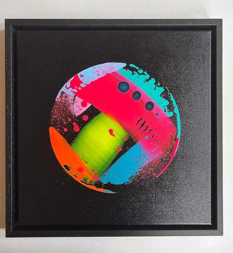 Pode incluir: Uma tela quadrada emoldurada apresentando uma pintura abstrata circular sobre um fundo preto. O design inclui pinceladas neon vibrantes em rosa, verde-lim&atilde;o, azul brilhante e laranja com efeitos de respingos e tr&ecirc;s pontos circulares azul-escuro.