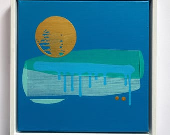 Puede incluir: Una pintura sobre lienzo cuadrada en un marco blanco con un fondo azul sólido. Un gran círculo dorado se sitúa sobre un bloque horizontal de pintura verde azulado y azul claro con goteos visibles. Dos pequeños puntos dorados están debajo.