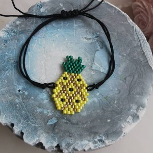 Puede incluir: Un brazalete de cuerda negra con un dije de piña de cuentas amarillas y verdes.