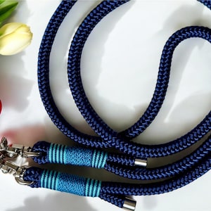 May include: A navy blue rope phone strap with silver-tone metal clasps. The strap features light blue and teal stripes near the clasps. The image also shows a red phone case and a few yellow tulips.