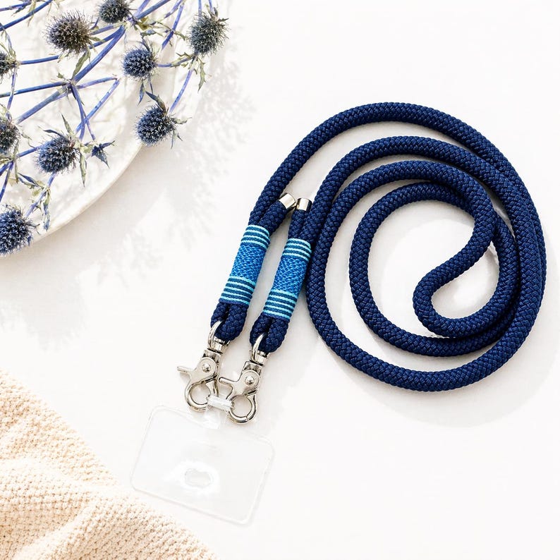 May include: A navy blue lanyard with a braided rope design. The lanyard has two blue and light blue striped accents near the metal clasps. A clear plastic ID holder is attached. The lanyard is on a white surface.