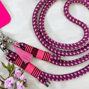 Könnte beinhalten: Eine geflochtene Hundeleine in Pink und Lila mit einem silbernen Karabinerhaken und einem rosa Quasten.