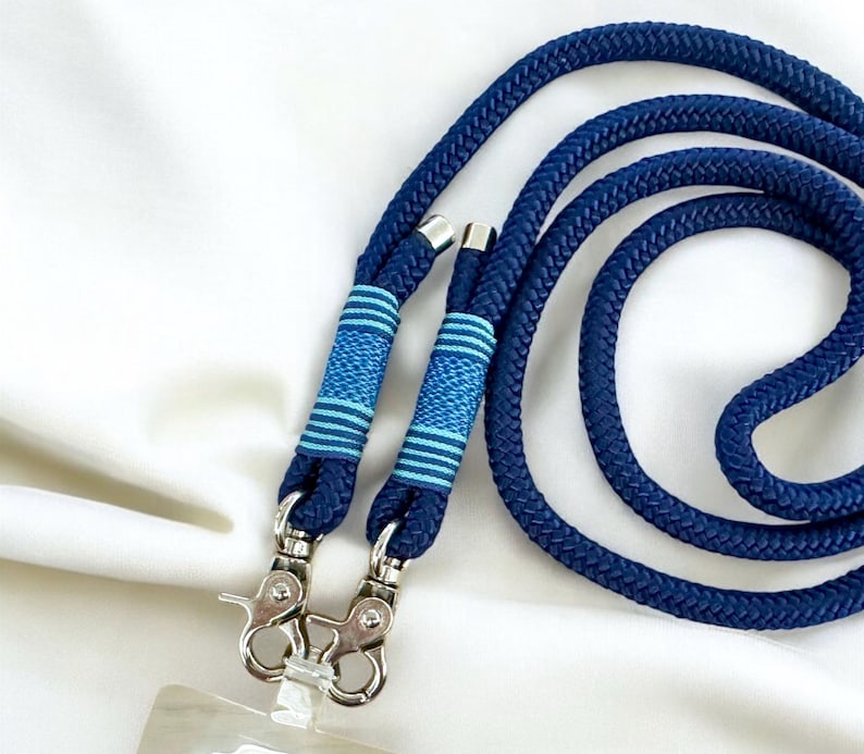May include: A navy blue lanyard with a thick, braided rope design. The lanyard features two silver-toned metal clasps and is accented with light blue and navy blue striped details. The lanyard is designed to hold an ID badge or other small items.