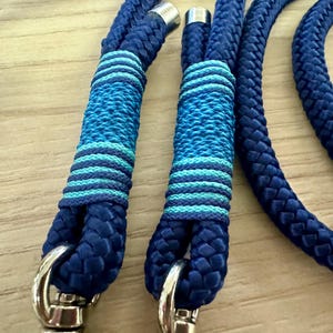 May include: Close-up of a blue rope leash with silver-colored metal hardware. The leash features decorative sections with alternating bands of light and dark blue. The rope is thick and appears durable.