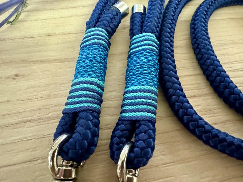 May include: Close-up of a blue rope leash with silver-colored metal hardware. The leash features decorative sections with alternating bands of light and dark blue. The rope is thick and appears durable.