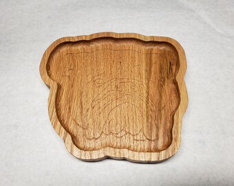 May include: A wooden tray shaped like a bulldog's head. The tray is made of light brown wood and has a smooth, polished finish.