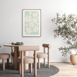 May include: A framed print of a stylized floral design featuring white flowers with yellow centers on a light green background. The print is hanging on a white wall above a dining table with four chairs.