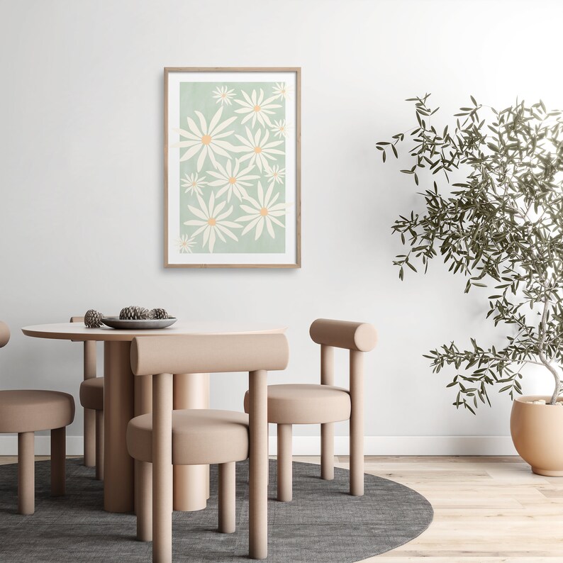 May include: A framed print of a stylized floral design featuring white flowers with yellow centers on a light green background. The print is hanging on a white wall above a dining table with four chairs.