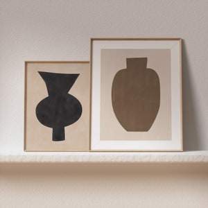 May include: Two framed prints with abstract vase silhouettes. The left print features a black vase on a beige background. The right print features a brown vase on a beige background.