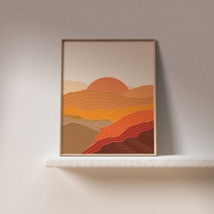 May include: A framed print depicting a sunset over a landscape of hills and valleys in shades of orange, yellow, and brown.