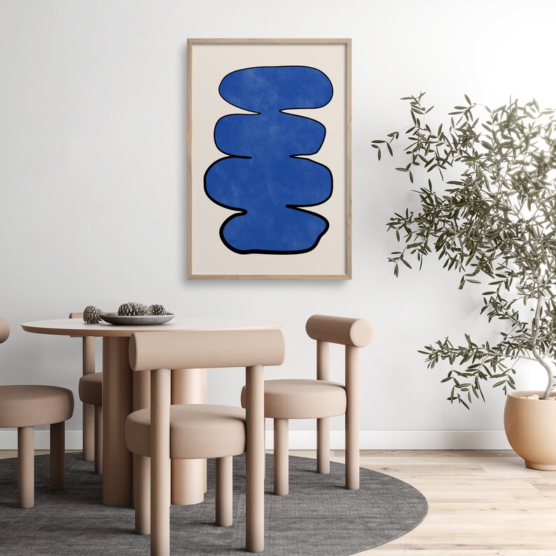 May include: Abstract art print featuring a stack of blue, organic shapes against a white background. The print is framed in a light wood frame and is hanging on a white wall.