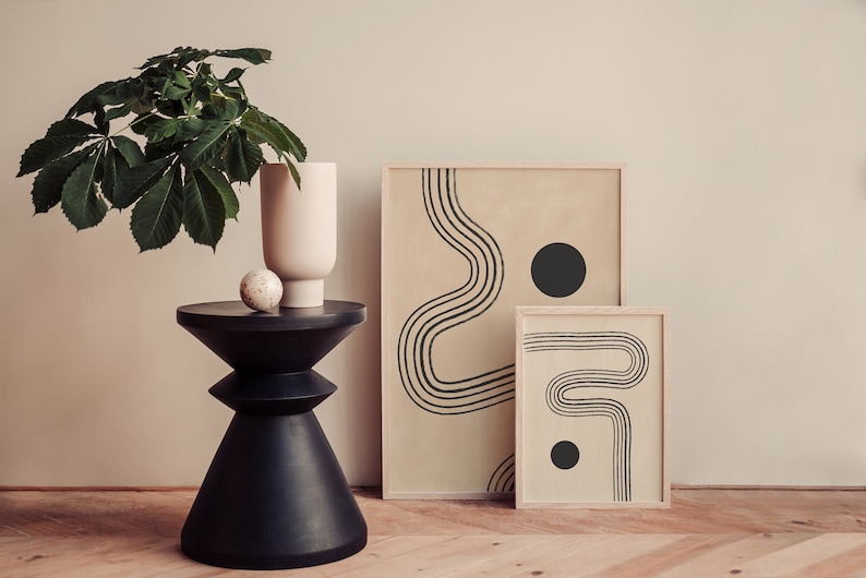 Puede incluir: Dos impresiones abstractas enmarcadas con l&iacute;neas negras y c&iacute;rculos sobre un fondo beige. Las impresiones est&aacute;n sobre una mesa de madera con un jarr&oacute;n negro y una planta verde.