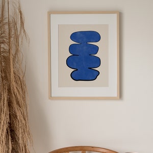 May include: A framed print of an abstract art piece featuring a blue, organic shape with a black outline against a beige background.