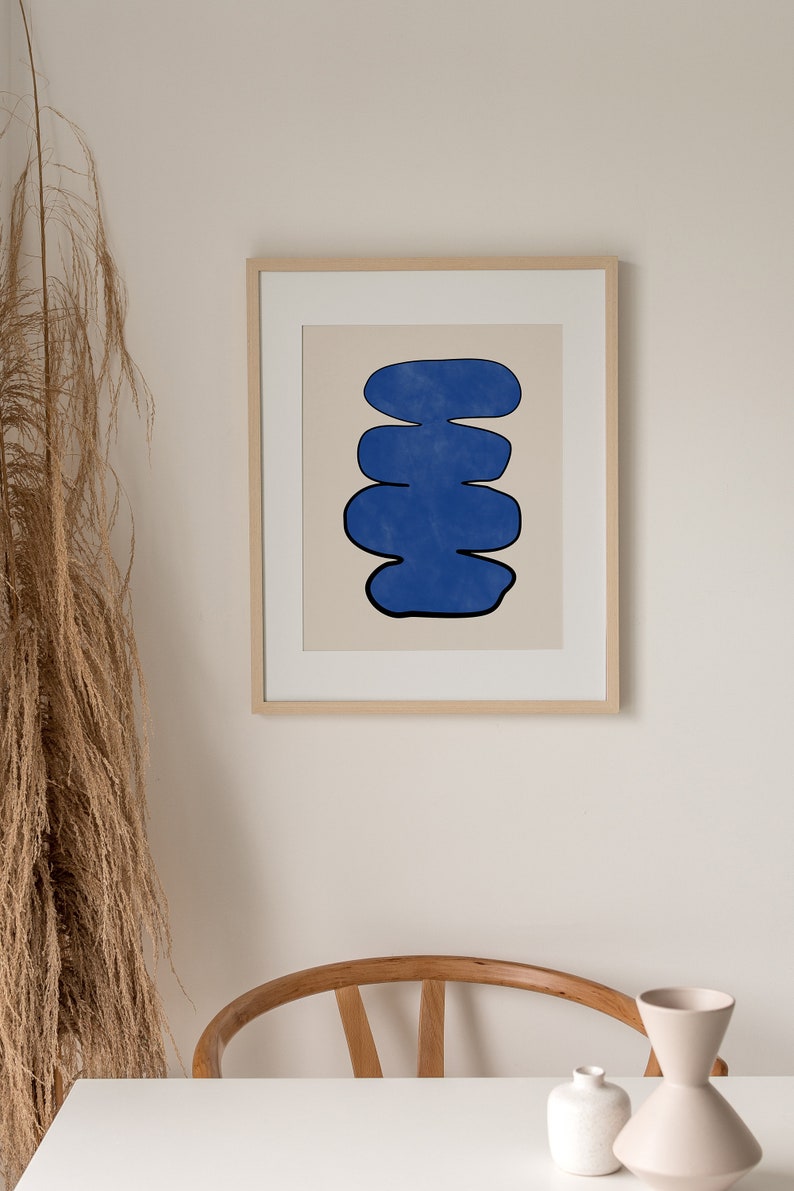 May include: A framed print of an abstract art piece featuring a blue, organic shape with a black outline against a beige background.