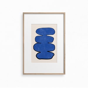 May include: A framed abstract print with a blue, organic shape resembling a stack of stones on a cream background.