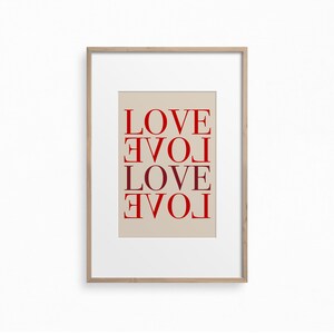 May include: A framed print with the word "LOVE" repeated four times in a vertical column, with each word rotated 90 degrees clockwise from the one above it. The words are in a red color on a beige background.