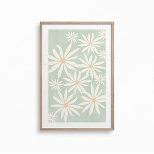May include: A framed print with a light green background and a pattern of white daisies with orange centers.