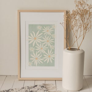 May include: A framed print of a floral design with white flowers on a light green background. The frame is made of light wood and is sitting on a white floor with a fluffy rug in front of it.